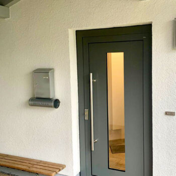 Haustüre aus Aluminium mit länglichem Glaseinsatz.